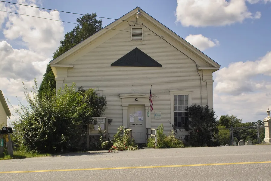 Photo: a white wooden town hall beside a road, with an American flag by the front door.